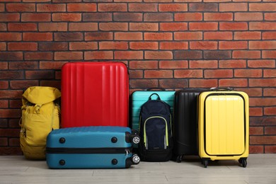 Photo of Many colorful suitcases and backpacks on floor near brick wall