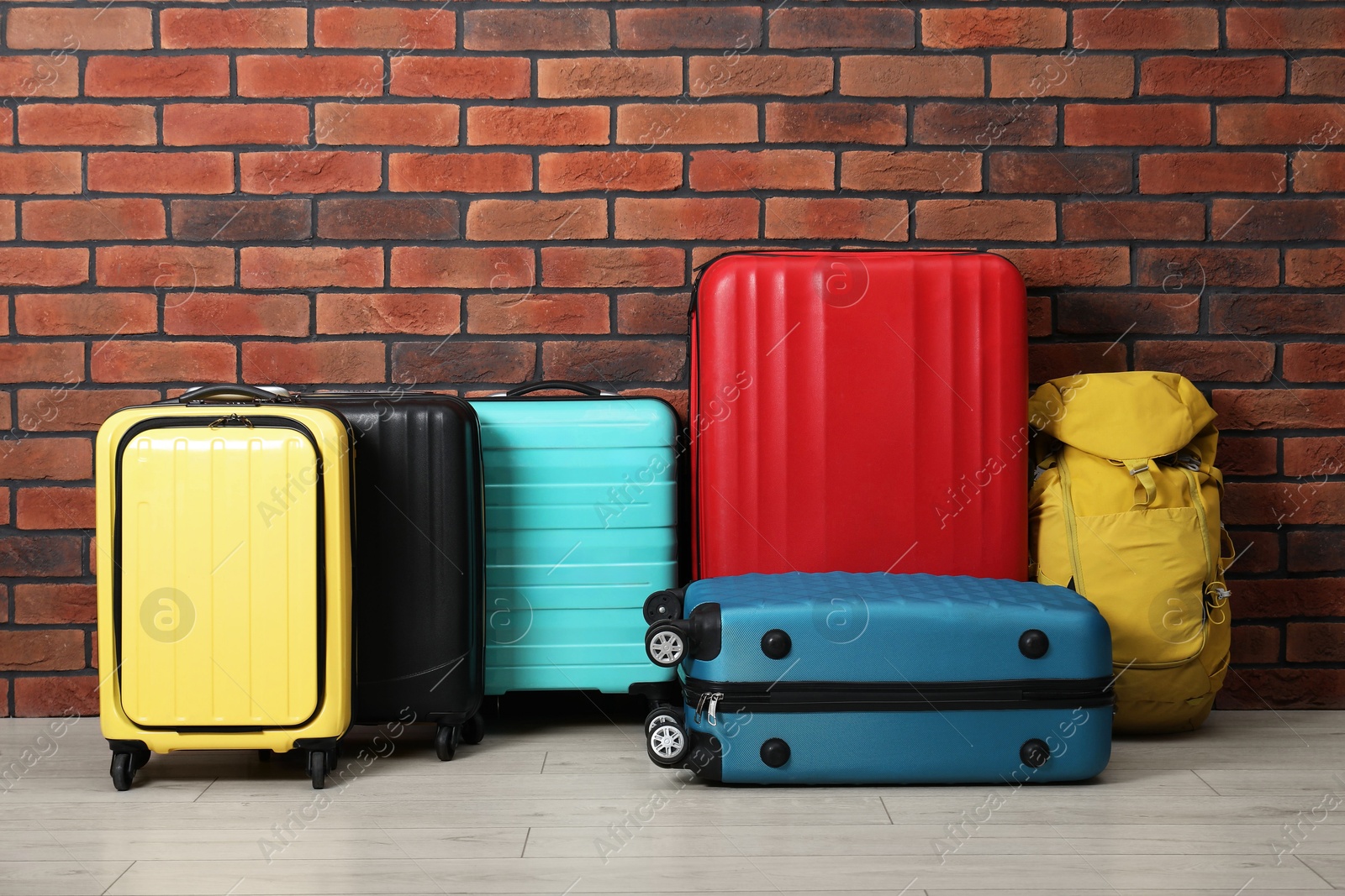 Photo of Many colorful suitcases and backpack on floor near brick wall