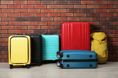 Photo of Many colorful suitcases and backpack on floor near brick wall