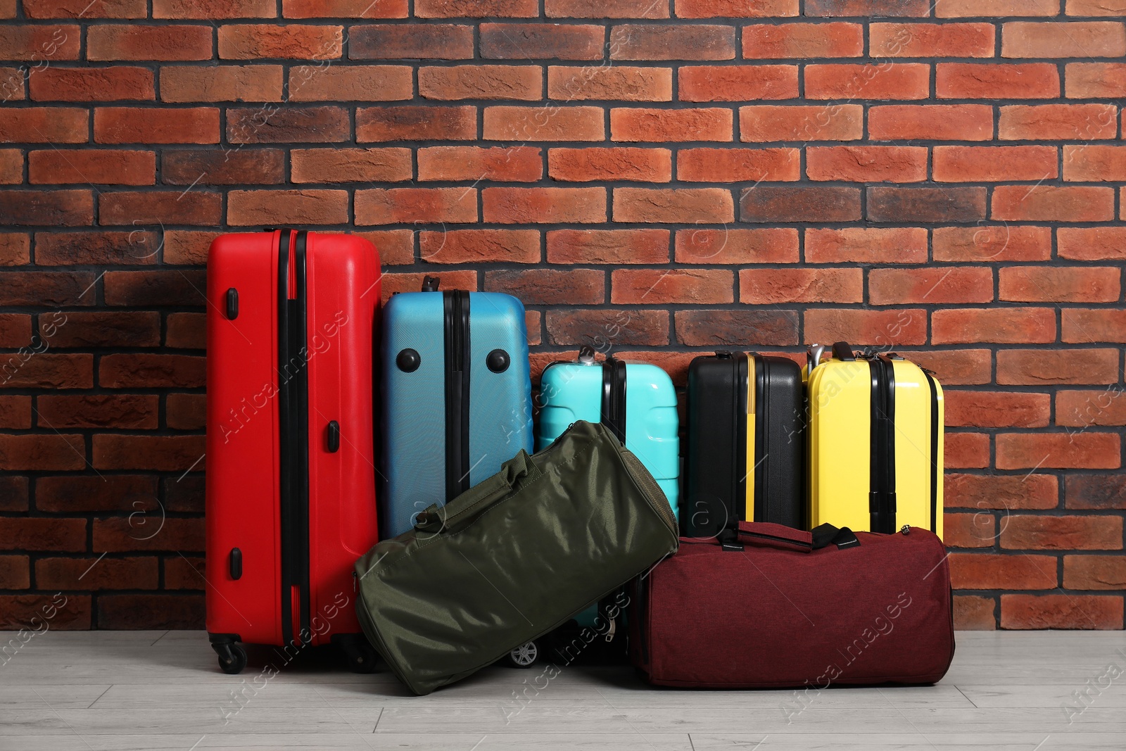 Photo of Many colorful suitcases and bags on floor near brick wall