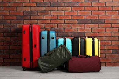 Photo of Many colorful suitcases and bags on floor near brick wall