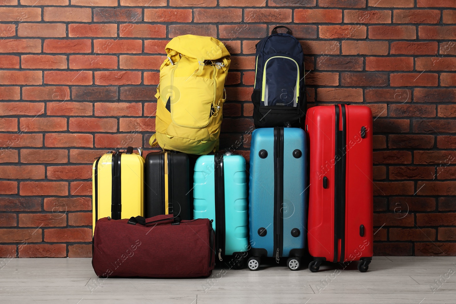 Photo of Many colorful suitcases, backpacks and bag on floor near brick wall