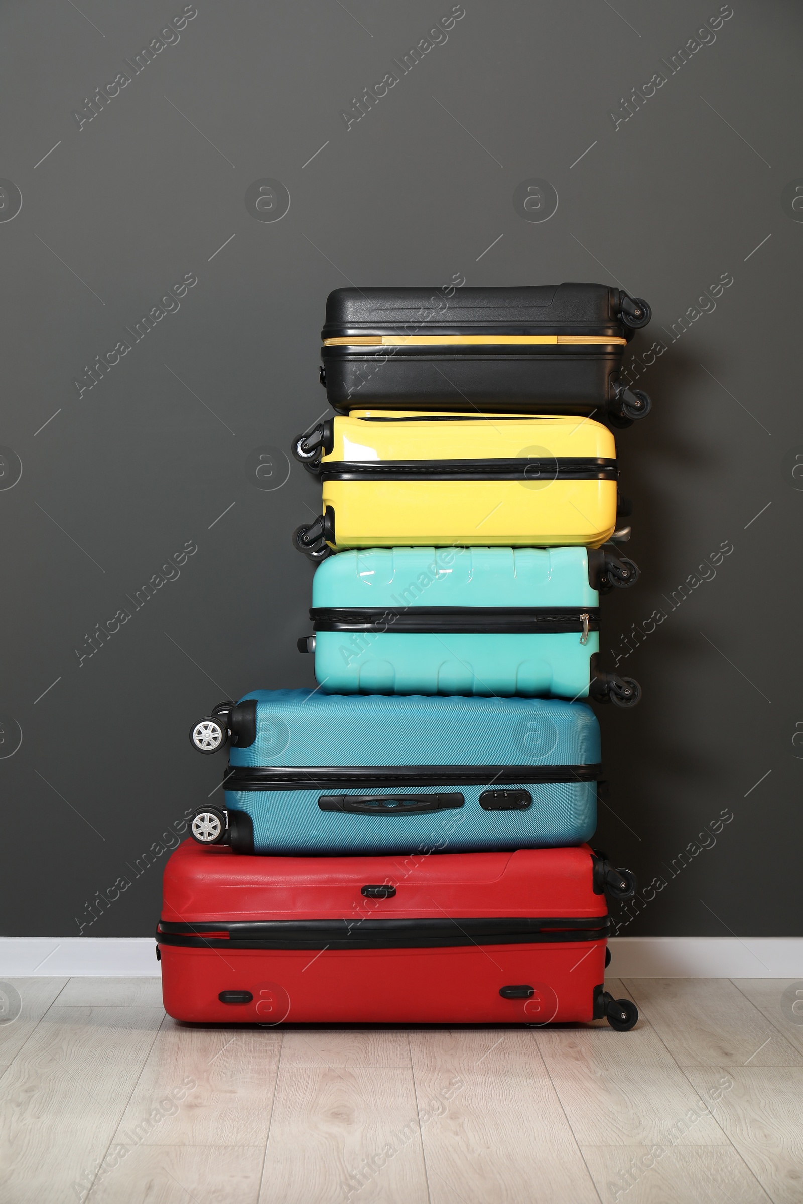 Photo of Stack of colorful suitcases on floor near black wall