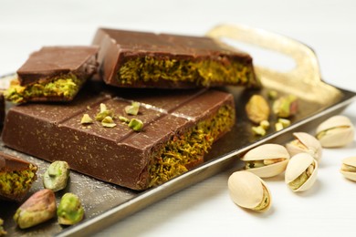 Photo of Pieces of Dubai chocolate bars with pistachios and knafeh on white table, closeup