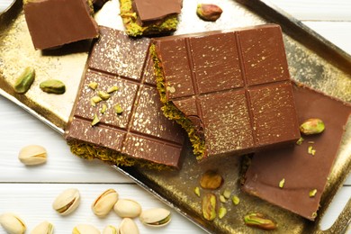 Photo of Pieces of Dubai chocolate bars with pistachios and knafeh on white wooden table, flat lay