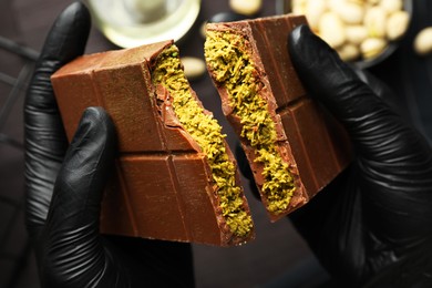 Photo of Woman breaking Dubai chocolate bar with pistachio and knafeh at table, closeup