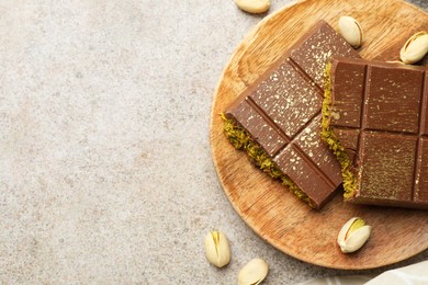 Photo of Pieces of Dubai chocolate bar with pistachios and knafeh on grey table, top view. Space for text