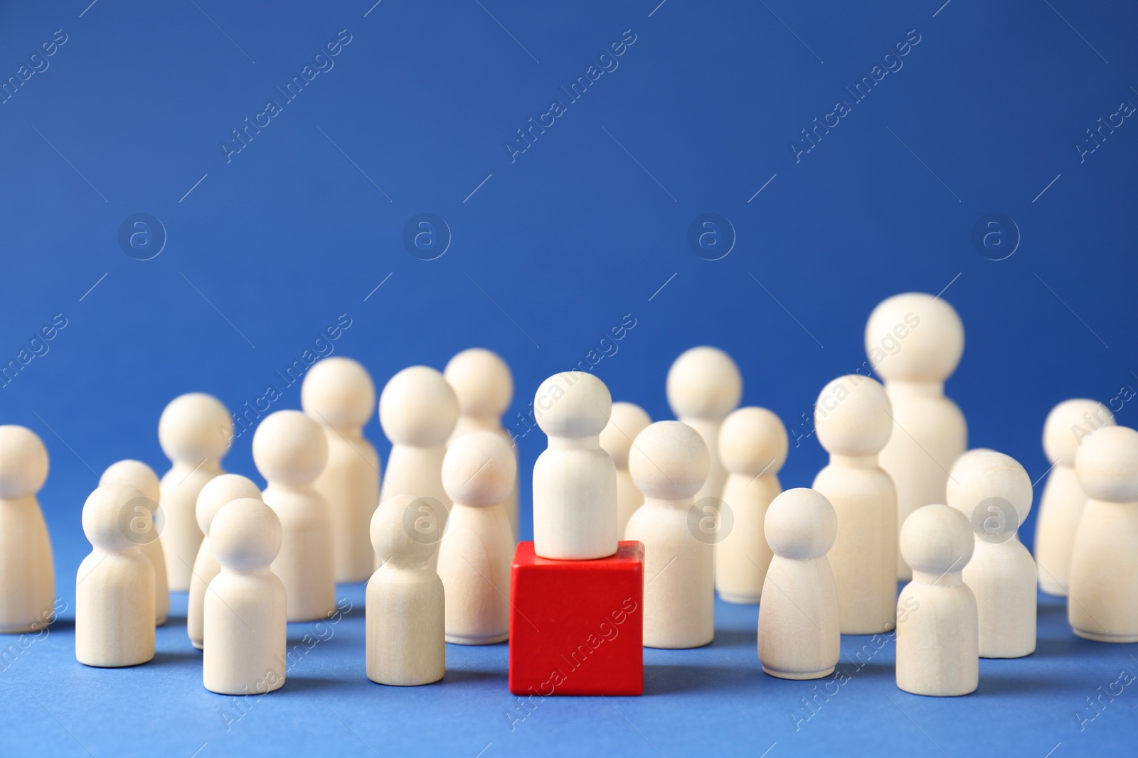 Photo of Competition concept. Human figure on wooden cube and other ones behind against blue background, closeup