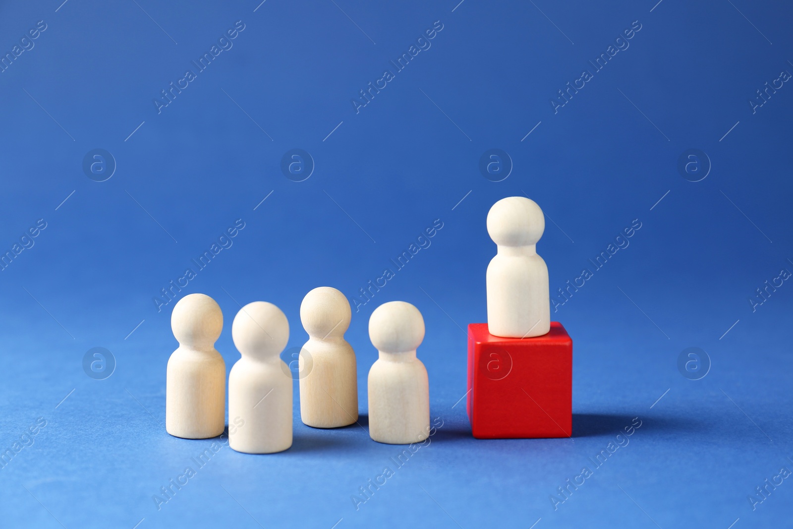 Photo of Competition concept. Human figure on wooden cube and other ones behind against blue background