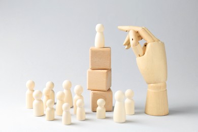 Photo of Competition concept. Human figure on wooden cubes, other ones behind and hand model against light background