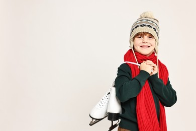 Photo of Little boy in hat with ice skates on light grey background, space for text