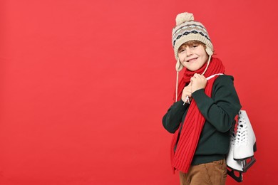 Photo of Little boy in hat with ice skates on red background, space for text