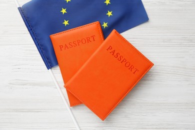 Photo of Passports in orange covers and flag of European Union on light wooden table, top view