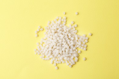 Photo of Pile of plastic granules on yellow background, top view