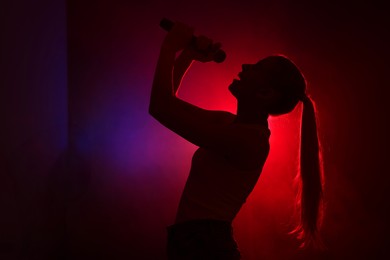 Photo of Silhouette of woman singing on dark background with color lights