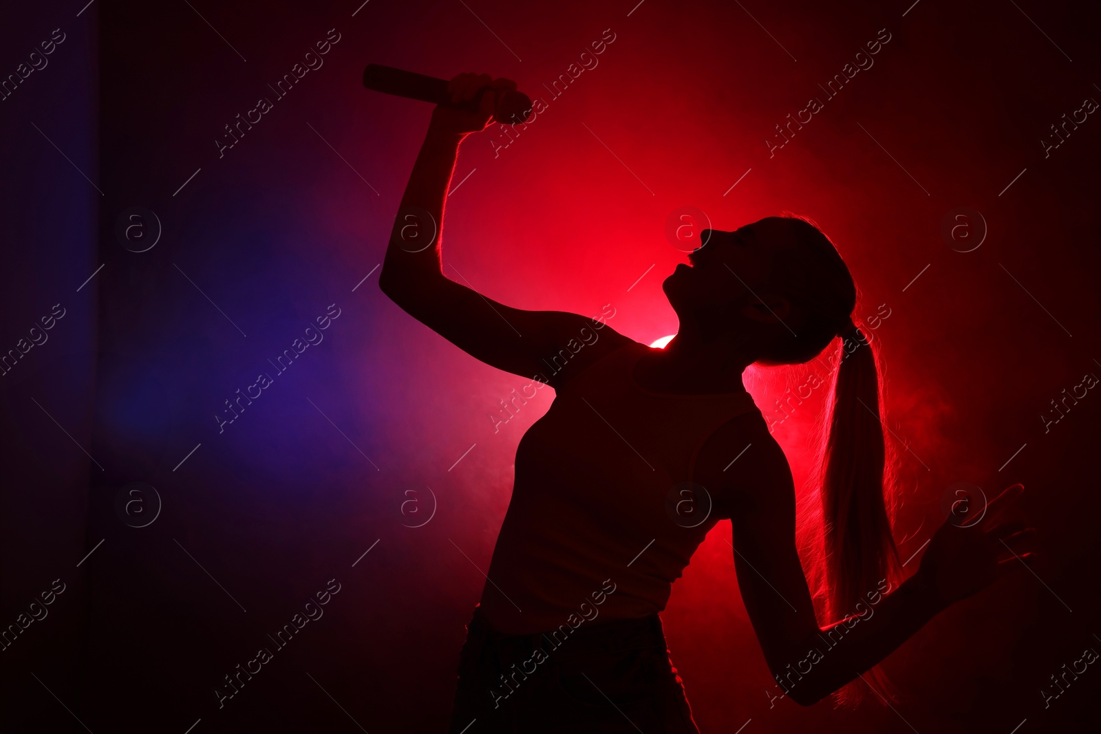 Photo of Silhouette of woman singing on dark background with color lights