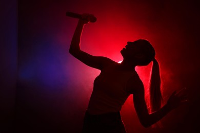 Photo of Silhouette of woman singing on dark background with color lights