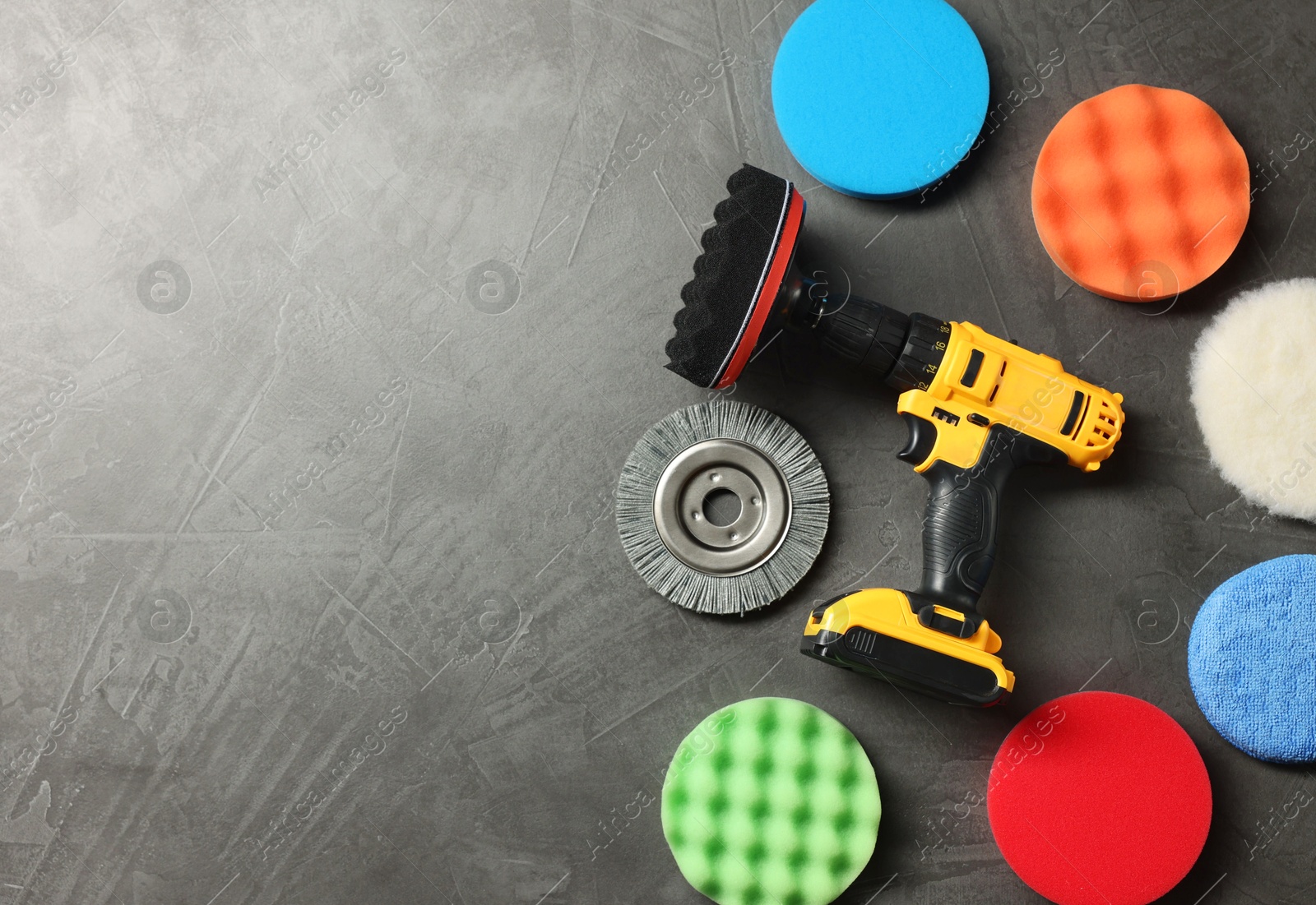 Photo of Electric screwdriver and polish pads on grey table, flat lay. Space for text