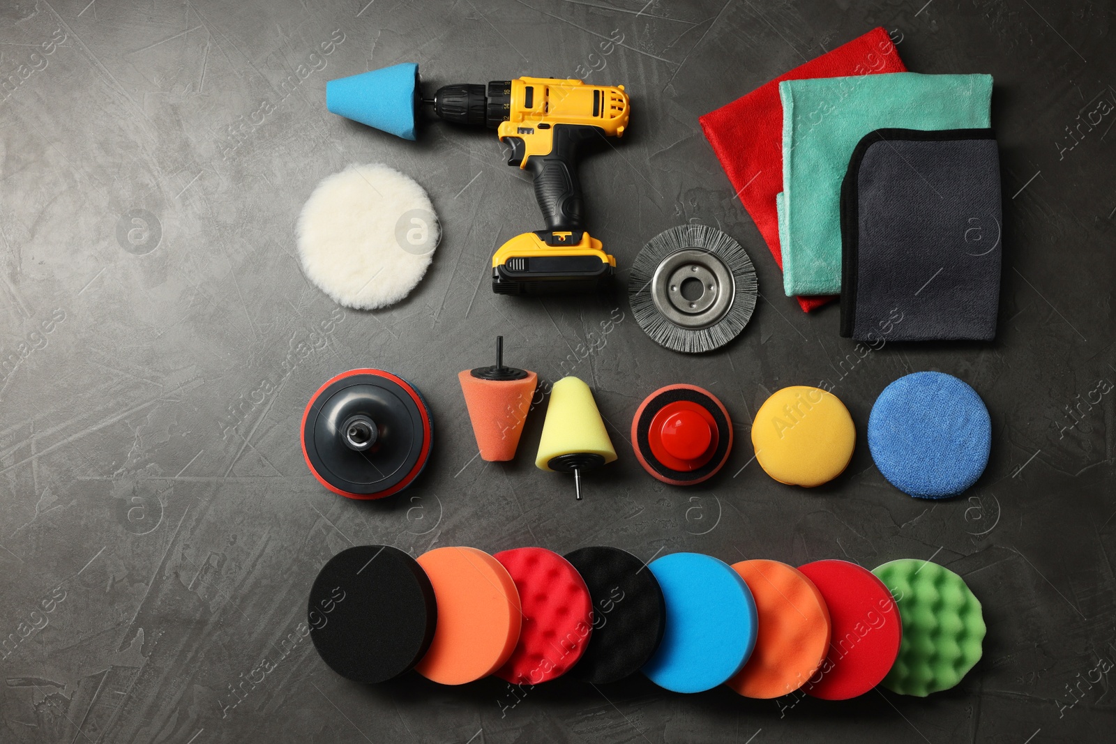 Photo of Different polish pads, electric screwdriver and rags on grey table, flat lay