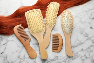 Photo of Set of different wooden brushes, combs and lock of hair on white marble table, flat lay