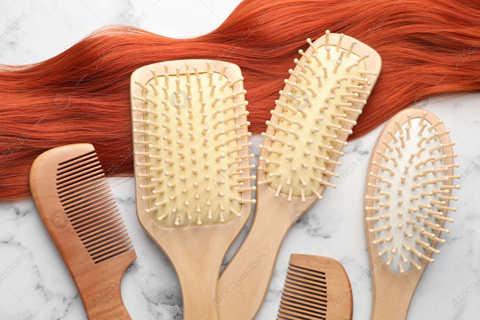 Photo of Set of different wooden brushes, combs and lock of hair on white marble table, flat lay