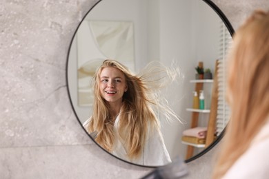 Photo of Beautiful young woman drying her hair near mirror in bathroom