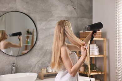 Photo of Beautiful young woman drying her hair in bathroom