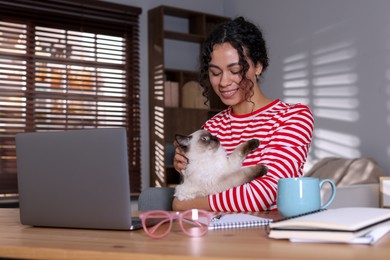 Photo of Beautiful woman with her cute cat working on laptop at desk in home office