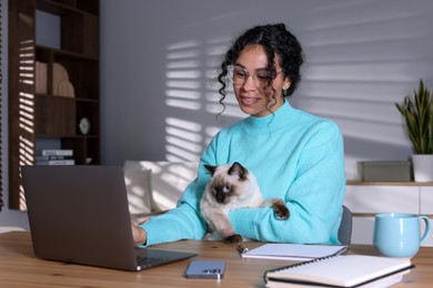 Photo of Beautiful woman with her cute cat working on laptop at desk in home office