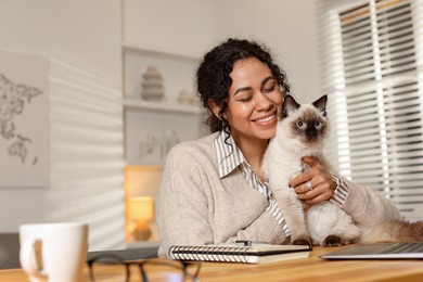 Photo of Beautiful woman with her cute cat working on laptop at desk in home office