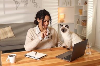 Photo of Beautiful woman with her cute cat working on laptop at desk in home office