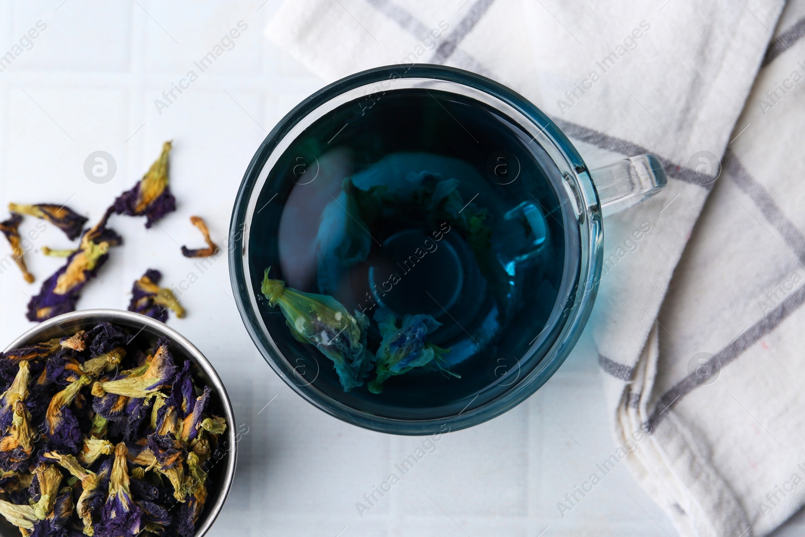 Photo of Delicious butterfly pea flower tea on white tiled table, flat lay