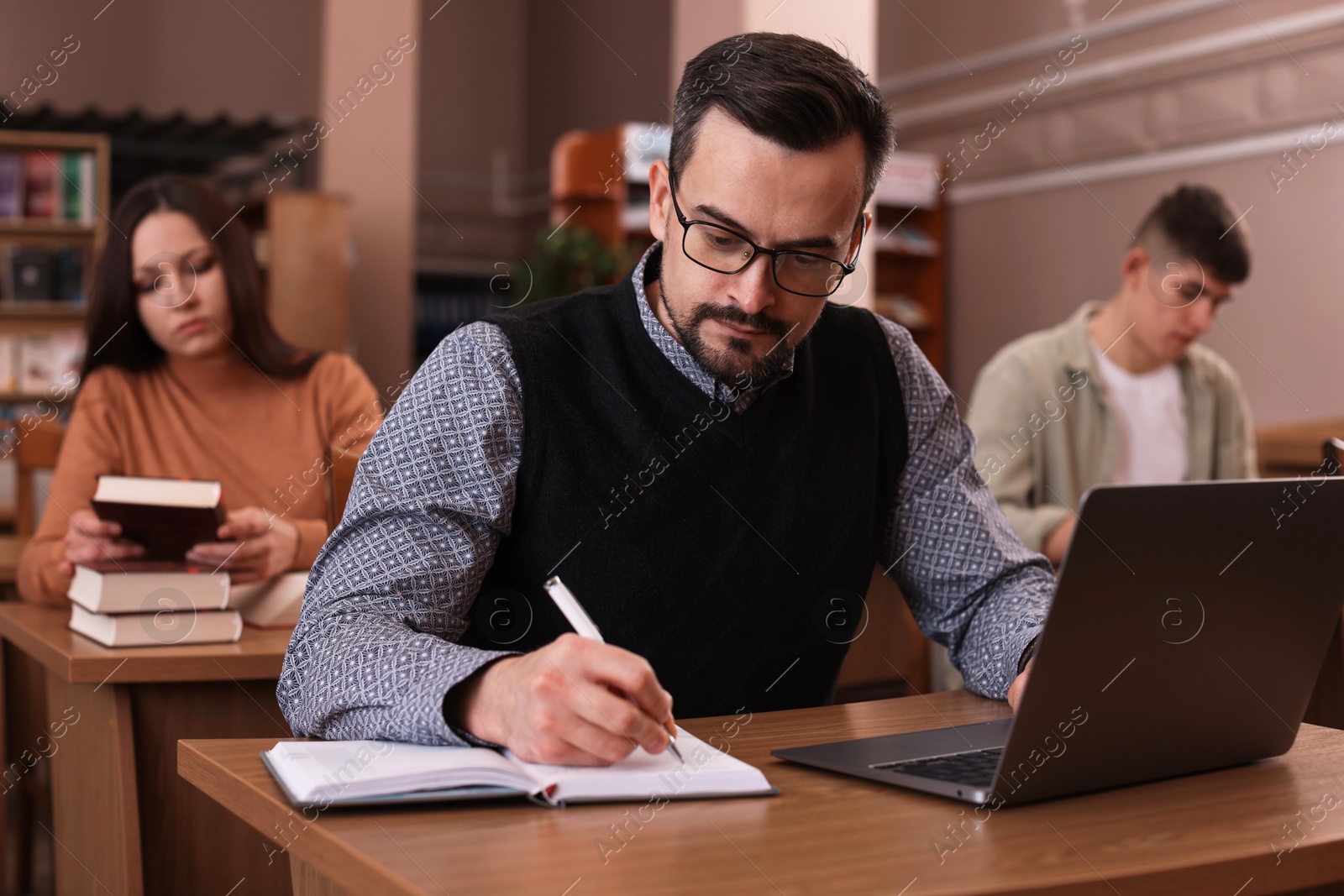 Photo of Man with laptop taking notes at desk in public library