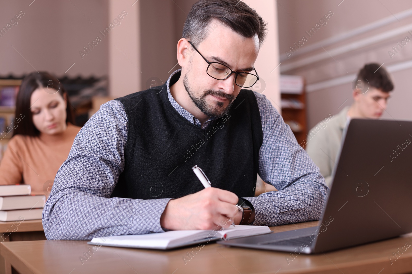 Photo of Man with laptop taking notes at desk in public library