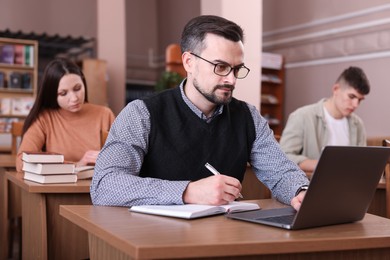 Photo of Man with laptop taking notes at desk in public library