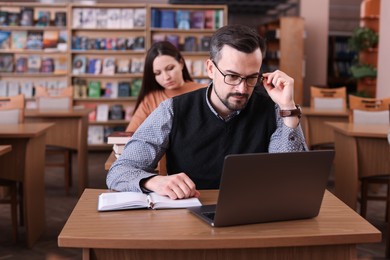 Photo of Man working with laptop at desk in public library