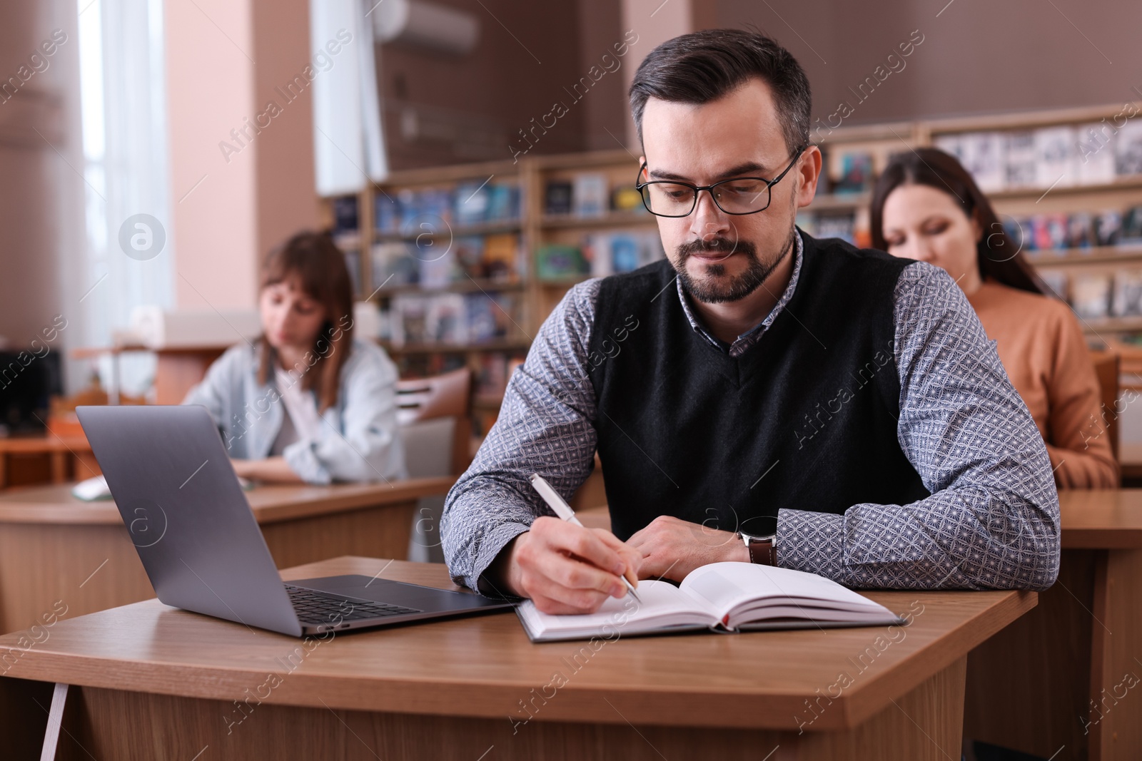 Photo of Man with laptop taking notes at desk in public library