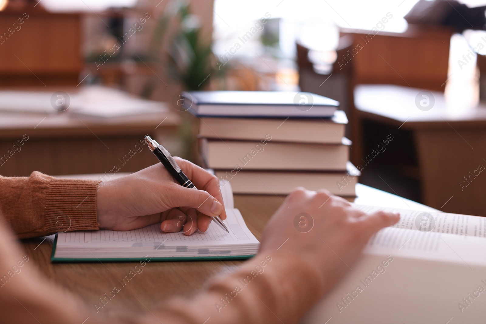 Photo of Woman reading book and taking notes at desk in library, closeup