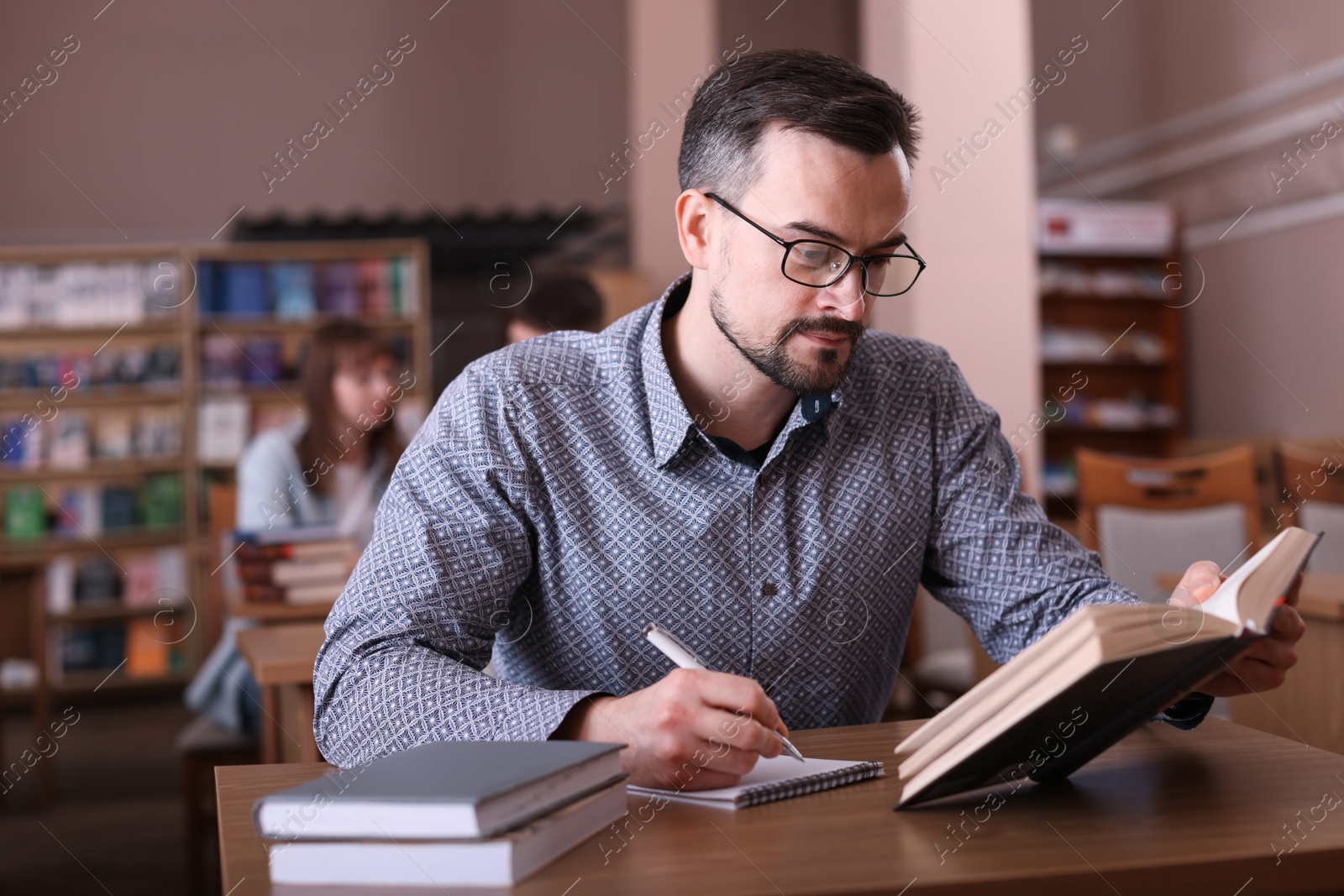 Photo of Handsome man reading book and taking notes at desk in public library