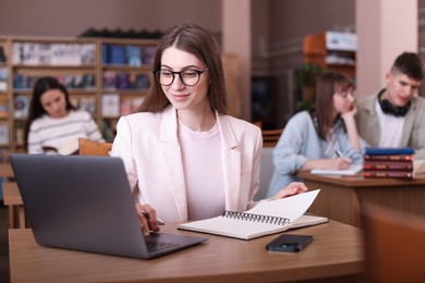 Photo of Beautiful woman with laptop taking notes at desk in public library