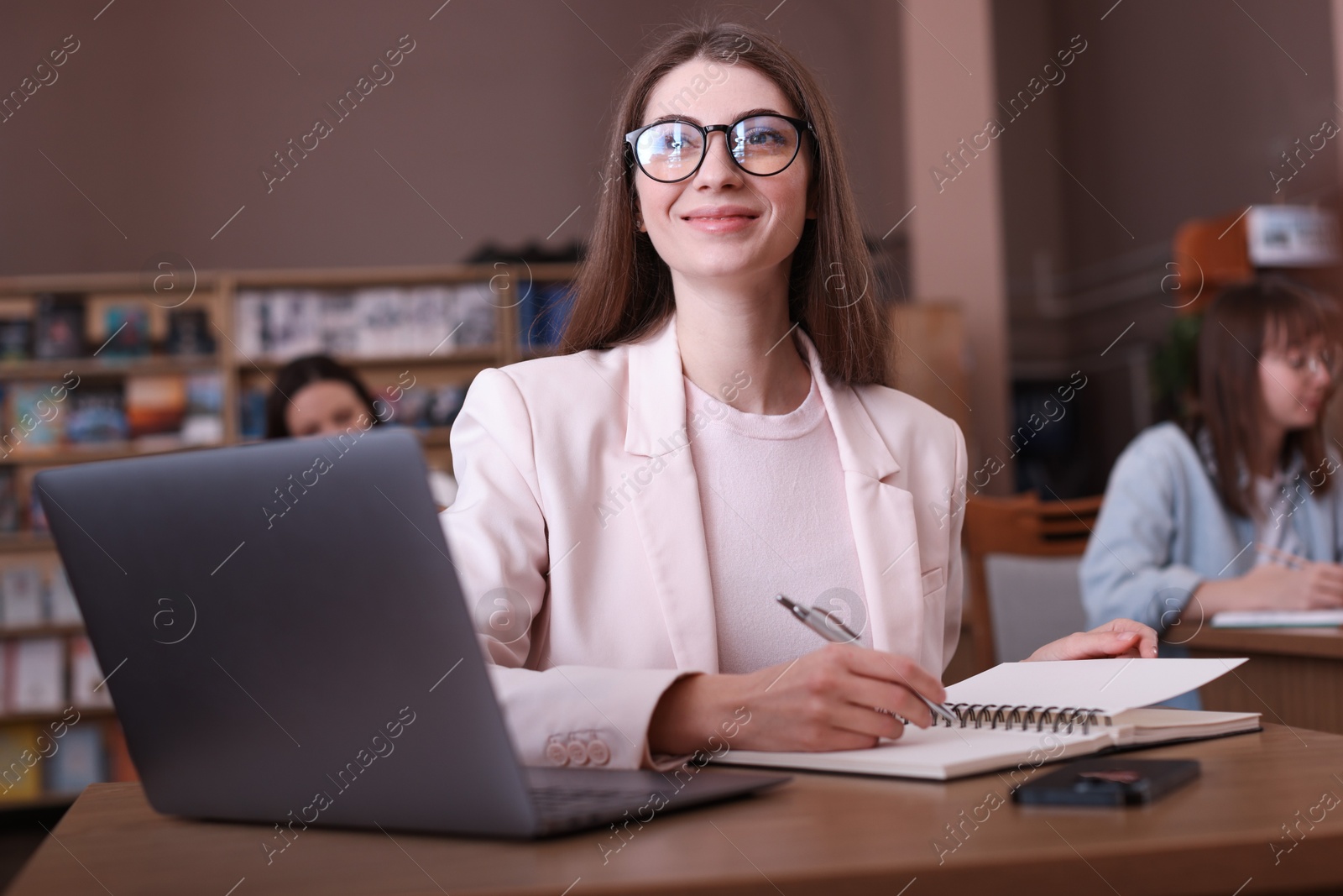 Photo of Beautiful woman with laptop taking notes at desk in public library