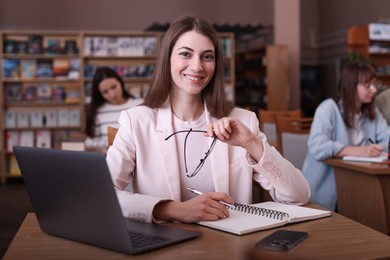 Photo of Portrait of smiling woman with laptop taking notes at desk in public library