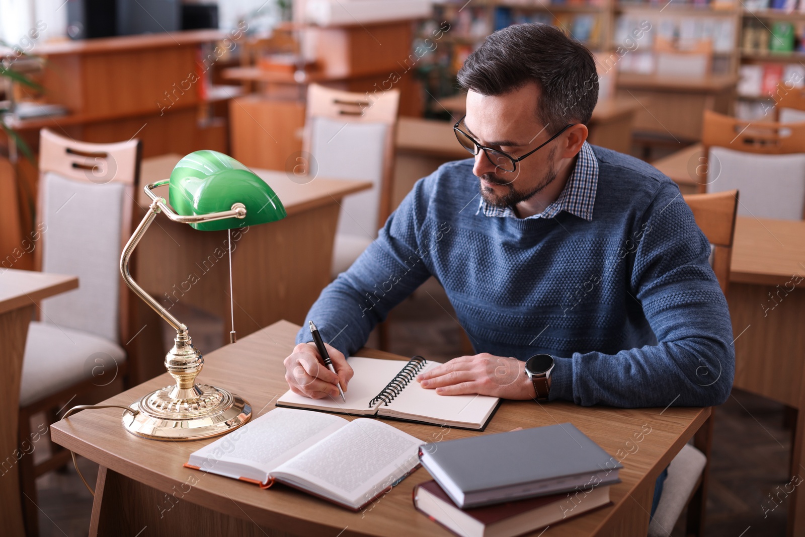 Photo of Handsome man reading book and taking notes at desk in library