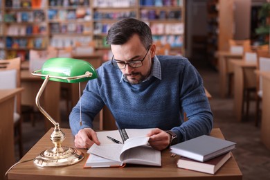 Photo of Handsome man reading book at desk in library