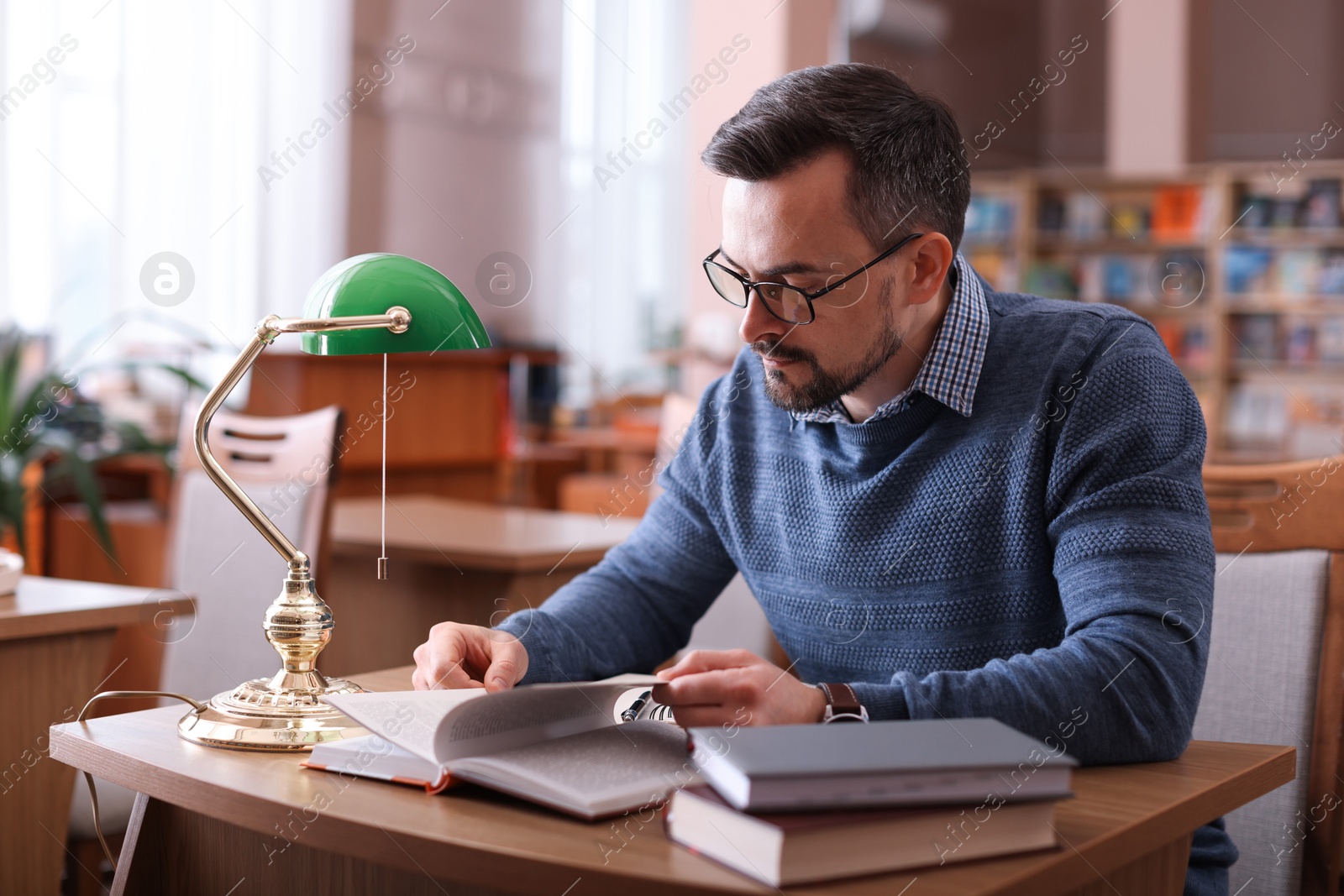 Photo of Handsome man reading book at desk in library