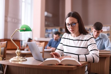 Photo of Beautiful woman working with book and laptop at desk in public library