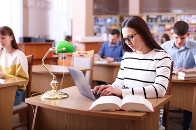 Photo of Beautiful woman typing on laptop at desk in public library