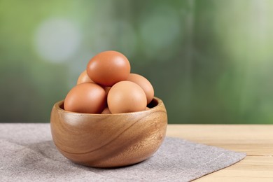 Photo of Raw eggs in bowl on wooden table, closeup. Space for text