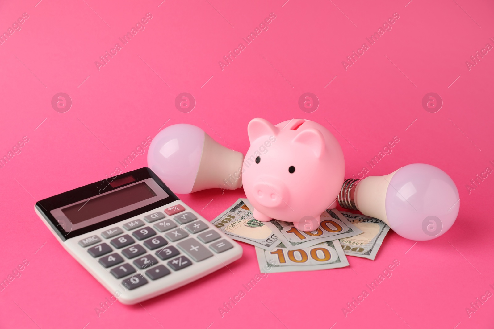 Photo of Piggy bank, dollar banknotes, calculator and light bulbs on pink background. Energy saving concept