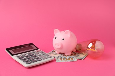 Photo of Piggy bank, dollar banknotes, calculator and light bulb on pink background. Energy saving concept